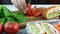 Woman cutting tomato on wooden board, sandwiches in lunch box on background. Preparation sandwiches for work, school