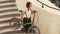 Woman cyclist walking down stairs and holding bicycle in arms. Woman bike city