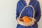 Woman in dark blue cotton shirt holds in hands wicker basket with small orange heirloom pumpkins white wall. Thanksgiving