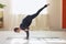 Woman in dark blue sportswear practicing yoga does handstand exercise with outstretched leg, Eka Pada Bakasana pose