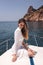 woman with dark hair in luxurious white dress relaxing on the deck of yacht, sailing in mediterranean sea