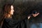 Woman with dark long hair in black robes is holding polished Shungite Sphere in her hands in front of the lake