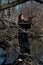 Woman with dark long hair in black robes standing on a tree stump in the middle of a swamp. Halloween and Gothic concept.