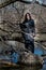 Woman with dark long hair in black robes standing on a tree stump in the middle of a swamp. Halloween and Gothic concept.