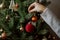Woman decorating christmas tree with red bauble closeup. Preparation for christmas time. Modern simple ornament in hands on