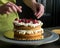Woman decorating a delicious sponge cake with icing cream and raspberries