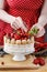 Woman decorating summer sponge cake with fruits on ceramic cake stand