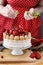 Woman decorating summer sponge cake with fruits on ceramic cake stand