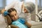 Woman dentist doing teeth checkup of little girl looks worried sitting in a dental chair visiting medical clinic.