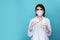 Woman dentist in the white mask with dental stuff isolatedin the blue studio.