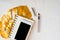 Woman desktop. Golden tropical monstera leaf, blank notepad, white smartphone and pen on white concrete background