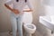 Woman with diarrhea standing in the bathroom, holding her stomach. Severe stomach pain, prepare to sit dung in the bathroom