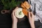 Woman dipping cracker into tasty creamy dill sauce at black wooden table, top view