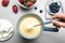 Woman dipping marshmallow into pot with white chocolate fondue at table