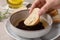 Woman dipping piece of bread into balsamic vinegar with oil and rosemary at table, closeup