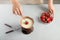 Woman dipping strawberry into bowl with white chocolate fondue on table