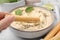 Woman dipping tasty grissini stick into hummus at light grey table, closeup