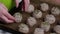 A woman dips a ball of dough in seeds and puts it on a baking sheet. Makes whole grain buns. Close-up