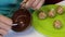 A woman dips a popcake billet into melted chocolate. Next to the plate are other blanks.