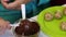 A woman dips a popcake billet in melted chocolate and shakes it. Next on the plate are ready-made blanks.