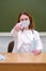 Woman doctor in a medical mask sits at a desk near a school board. The problem with lessons in the classroom during the virus