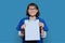 Woman doctor pointing with finger at blank paper on clipboard, blue background