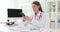 Woman doctor sits at desk and types message on smartphone