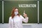 Woman doctor stands at the school board with the text vaccination. The problem with lessons in the classroom during the virus