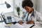 Woman doctor with stethoscope looking at medical papers at her office working hard