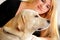 Woman with dog is resting in bed at home, relaxing in bedroom. Girl is petting with her dog. Portrait of cute yellow labrador.