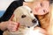 Woman with dog is resting in bed at home, relaxing in bedroom. Girl is petting with her dog. Portrait of cute yellow labrador.