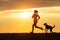 Woman and dog running on beach at sunset