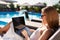 Woman doing remote multitasking work with multiple electronic internet devices on swimming pool beach bed. Freelancer