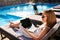 Woman doing remote multitasking work with multiple electronic internet devices on swimming pool beach bed. Freelancer