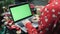 Woman is doing shopping online on laptop with chroma key green screen sitting at home in front of Christmas tree. Female is buying
