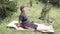 woman doing stretching and yoga on a bamboo rug in the middle of the garden with green grass and plants that swing in the