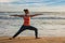 Woman doing yoga asana Virabhadrasana 1 Warrior Pose on beach on