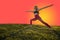 Woman Doing Yoga on Grass in Warrior 2 Pose With Copy Space Orange Background