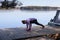 Woman doing yoga on the lake, relaxing in nature. Wooden float pier with motorboat, calm water