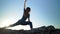 Woman doing yoga Virabhadrasana - warrior pose on high hill, sky background, sunset time. Stretching, everyday practice