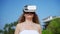 Woman dons VR headset, exploring immersive tropical beach environment. Engages with digital realm, palm trees sway