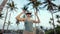 Woman dons VR headset among palm trees, enters digital realm. Experiencing virtual environment, she reaches out