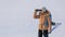 Woman in down jacket with a backpack and ski poles in hand looks through binoculars standing on a snowy plain in winter
