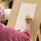 Woman draws at art studio for elderly people, easel with blank paper.