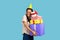 Woman with dreadlocks, posing in party cone, holding embracing stack of presents, happy birthday.
