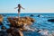 Woman in dress dancing on rock. Waves crashing on stones. Virgin nature, summer holiday and beach concept. Copy space