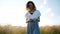 Woman in a dress with a grass in her hand walks in a field at sunset, slow motion and camera movement