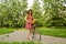 Woman in a dress and hat with a bike with flowers in a basket in a summer park