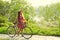 Woman in a dress and hat with a bike with flowers in a basket in a summer park