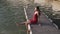 Woman in dress sitting on wooden pier, swings her feet in water, slow motion